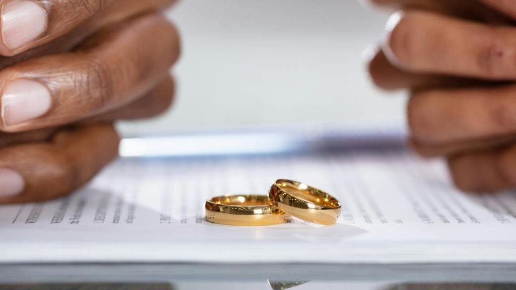 Two people going through divorce with their wedding rings on top of divorce papers