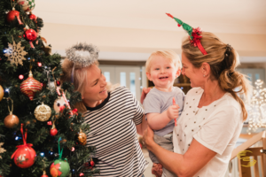 A grandmother and mother celebrating Christmas with their young child by a decorated tree, highlighting family connections and shared holiday traditions during co-parenting at Christmas.