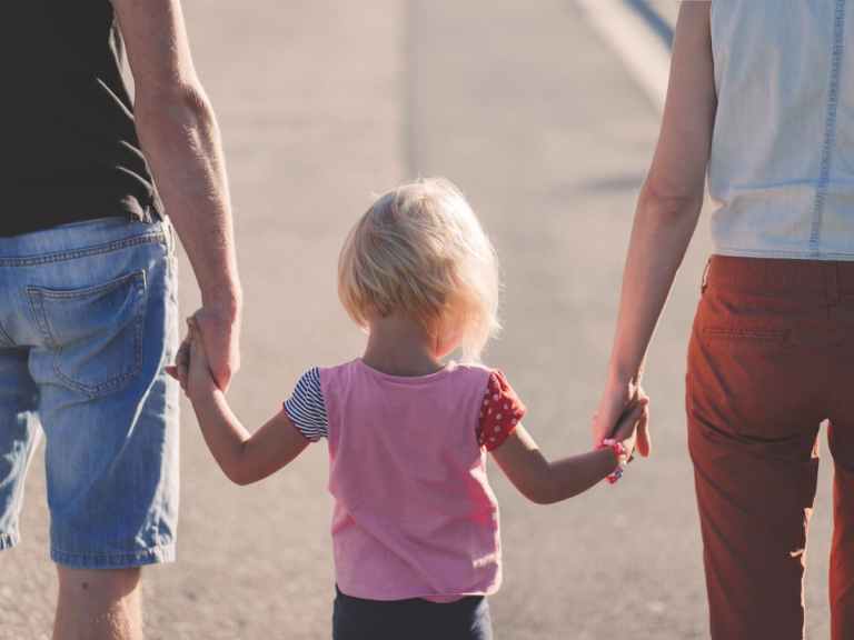 Co-parents holding their child's hands while walking down road