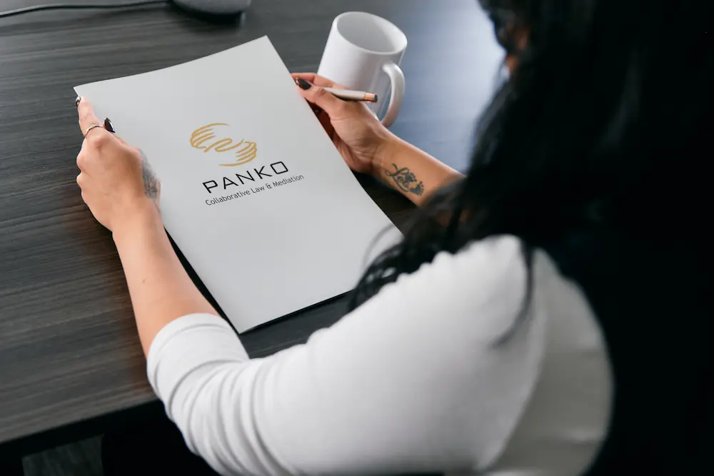 A woman with a coffee mug reads a Panko Collaborative Law brochure at a dark wooden desk.